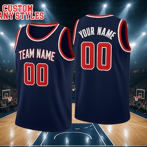 May include: A navy blue basketball jersey with red and white trim. The front features the text TEAM NAME and the number 00 in red with white outlines. The back displays YOUR NAME and the number 00 in white. The text CUSTOM ANY STYLES is visible.