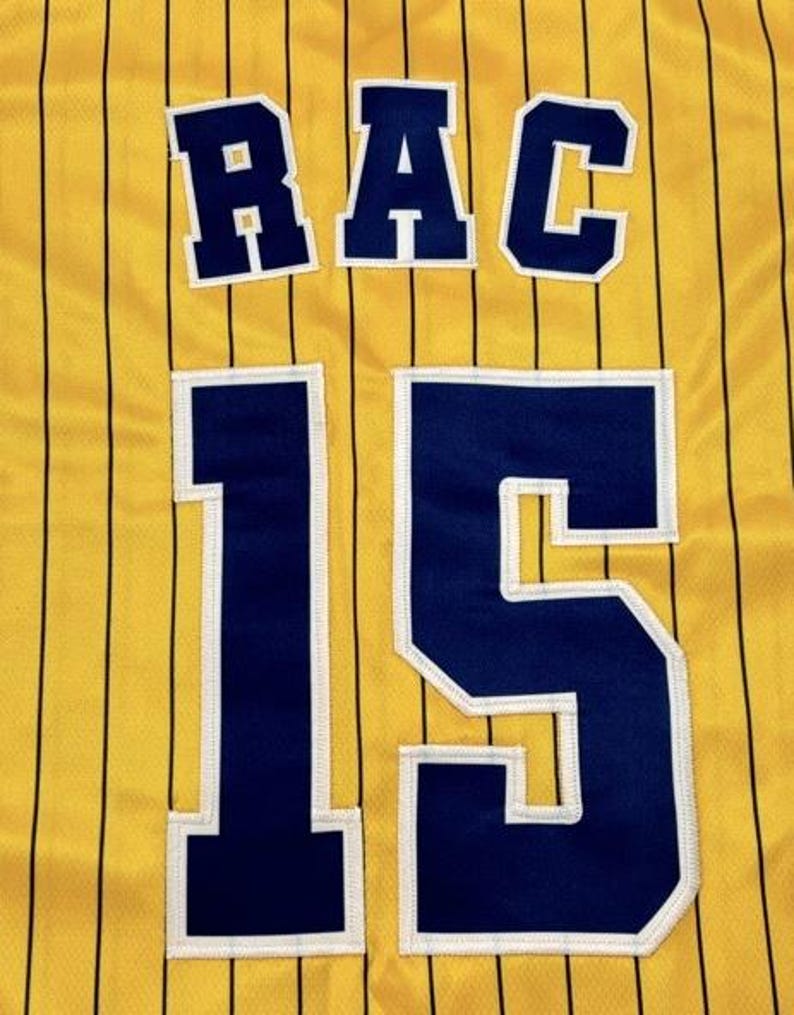 May include: A yellow athletic jersey featuring thin vertical black pinstripes. The back displays the letters RAC in dark blue with white trim, positioned above the large number 15, also rendered in dark blue with white trim.