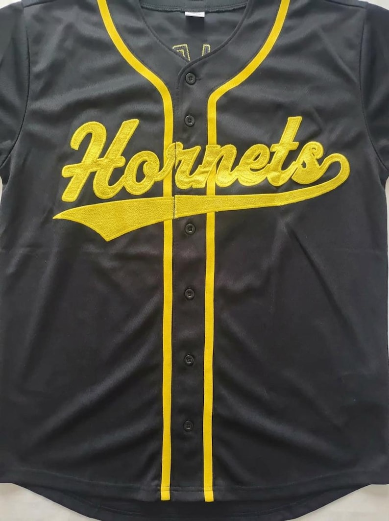 May include: A black baseball jersey featuring a button-down front with yellow piping along the placket and collar. The word "Hornets" is embroidered in yellow script across the chest, with a yellow underline extending from the letter s.