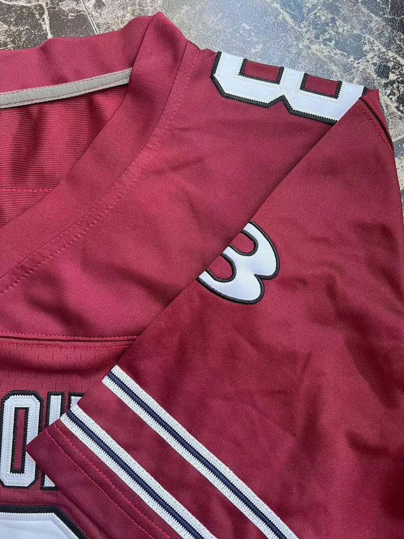 Puede incluir: Camiseta deportiva granate con detalles en blanco y azul marino. La camiseta lleva el n&uacute;mero "3" en blanco con contorno negro en la manga y el hombro. La camiseta tiene cuello en V y una raya blanca en el cuello.