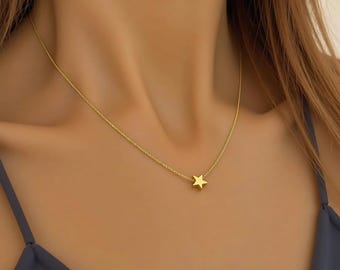 May include: A delicate gold-colored necklace featuring a small star pendant. The chain is thin and the star is centered, creating a minimalist and elegant design. The necklace is worn close to the neck.