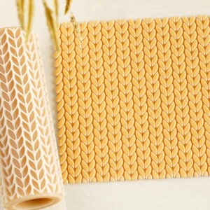 May include: A cylindrical rolling pin and a square flat sheet, both featuring a raised, repeating knit-like texture. The objects are light beige in color and display a consistent pattern of interlocking vertical loops across their surfaces.