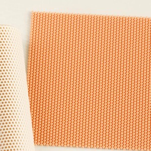 May include: A cylindrical roll of off-white material featuring a uniform honeycomb grid pattern and a flat, square sheet of peach-colored material with a dense, raised circular dot texture arranged in a precise grid across the entire surface.