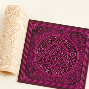 May include: A cylindrical beige rolling pin featuring an engraved celestial pattern of stars, crescents, and geometric shapes, alongside a square purple tile displaying the same intricate embossed design in a darker shade of magenta.