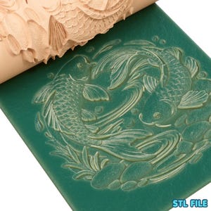 May include: A beige rolling pin with a koi fish pattern is pressed into a green surface, creating a detailed relief. The design features two koi fish swimming among aquatic plants and stones. The text "STL FILE" is visible in the bottom right corner.