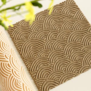May include: A brown rolling pin with a raised pattern of overlapping arches. The rolling pin is made of a textured material and is designed for creating decorative patterns in dough.