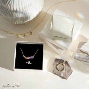 K&ouml;nnte beinhalten: Eine Sammlung von Goldschmuck, darunter Halsketten und Ringe, wird auf einer wei&szlig;en Oberfl&auml;che pr&auml;sentiert. Eine Halskette hat einen Kreuzanh&auml;nger, w&auml;hrend eine andere farbige Edelsteine aufweist. Ein goldener Ring liegt auf einem Stein.