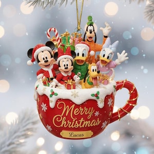 May include: A festive red Christmas mug ornament featuring Disney characters Mickey, Minnie, Donald, Daisy, Goofy, and Pluto. The mug is inscribed with "Merry Christmas" and "Lucas". The ornament is decorated with holly and snow, hanging from a snowy branch.