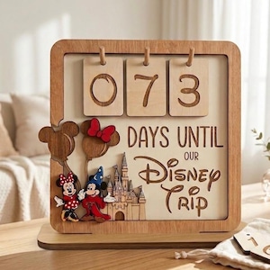 May include: A wooden countdown calendar featuring the text "DAYS UNTIL OUR DISNEY TRIP" with three hanging wooden number tiles displaying "073". The sign includes laser-cut wooden figures of Mickey and Minnie Mouse and a castle.