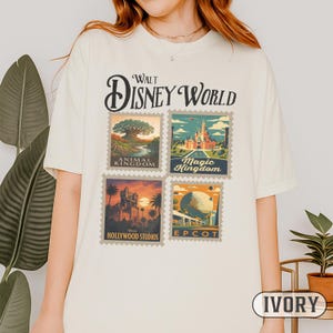 May include: Ivory-colored t-shirt featuring a vintage-style design with the text "Walt Disney World." The design includes four postage stamp-like images representing Animal Kingdom, Magic Kingdom, Hollywood Studios, and Epcot. The shirt is a relaxed fit.