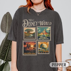 May include: Dark gray t-shirt featuring the words "Walt Disney World" above four postage stamp designs. The stamps depict Animal Kingdom, Magic Kingdom, Hollywood Studios, and Epcot. The word "Pepper" is printed at the bottom.