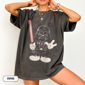 Pu&ograve; includere: T-shirt grigio scuro con un personaggio dei cartoni animati di Darth Vader con le orecchie di Topolino, che tiene una spada laser rossa. La grafica &egrave; in nero, grigio e bianco. La parola "PEPPER" &egrave; in un rettangolo bianco in basso.