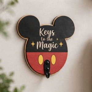 Può includere: Un gancio da parete per chiavi in legno a forma di testa di topo. La parte superiore è nera, quella inferiore è rossa con due ovali gialli. Presenta la scritta "Keys to the Magic" in lettere bianche, accentuata da quattro piccole stelle.