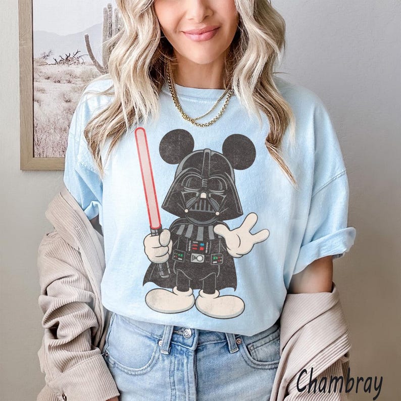 Pu&ograve; includere: T-shirt azzurra con un personaggio dei cartoni animati di Darth Vader con le orecchie di Topolino, che tiene una spada laser rossa. La grafica &egrave; in bianco, nero e grigio. La maglietta ha una vestibilit&agrave; ampia.
