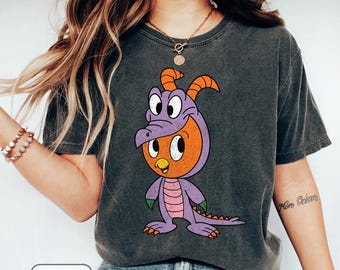 May include: Dark gray t-shirt featuring a cartoon character in a purple and orange dragon costume. The character has large white eyes and is standing. The word "PEPPER" is printed at the bottom of the image.