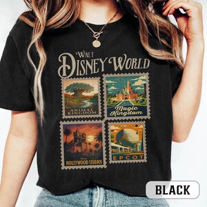 May include: Black t-shirt featuring a Walt Disney World design. The design includes four postage stamp-style images representing Animal Kingdom, Magic Kingdom, Hollywood Studios, and Epcot. The shirt also has the word "BLACK" printed on it.