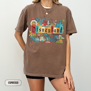 K&ouml;nnte beinhalten: Espressofarbenes T-Shirt mit einem farbenfrohen Disneyland Resort-Grafik. Das Design umfasst verschiedene Parksymbole und das Disneyland-Logo. Das Shirt hat kurze &Auml;rmel und eine lockere Passform, geeignet f&uuml;r den t&auml;glichen Gebrauch.
