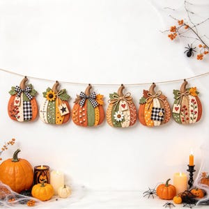 May include: A decorative garland featuring six hanging wooden pumpkin ornaments in various autumn colours, patterns, and embellishments like bows, leaves, and tags. Below, several real pumpkins, lit candles, and artificial spider webs are arranged.