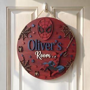 May include: A circular wooden wall sign with a dark red stained finish featuring a layered Spider-Man mask at the top and a full-body Spider-Man figure below. The text reads Oliver's Room in blue and white, accented by spider webs and stars.
