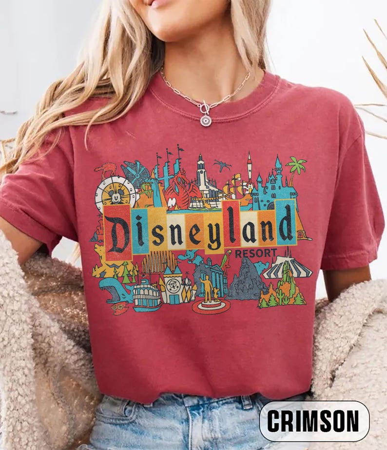 K&ouml;nnte beinhalten: Karmesinrotes T-Shirt mit einem farbenfrohen Disneyland Resort-Grafik. Das Design zeigt ikonische Parkbilder und das Disneyland-Logo in einem Retro-Stil. Das Shirt ist bequem und l&auml;ssig.