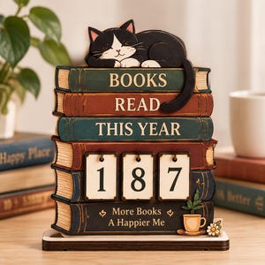 May include: A decorative wooden book stack display featuring a black and white cat resting on top. The spines are labelled BOOKS READ THIS YEAR with three flip-style number cards showing 187 and the text More Books A Happier Me with a coffee cup.