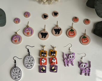 Könnte beinhalten: Eine Auswahl an Halloween-Ohrringen mit Geister-, Katzen-, Kürbis- und Hexenmotiven. Die Ohrringe sind in verschiedenen Farben erhältlich, darunter Lila, Orange, Schwarz und Weiß. Einige sind Ohrstecker, andere sind Hängeohrringe.