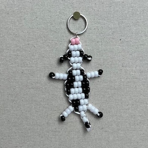 May include: A black and white beaded cow keychain with a pink nose and a silver key ring.
