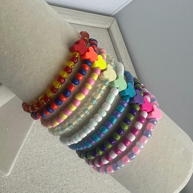 May include: A collection of colorful beaded bracelets. Each bracelet features a different color scheme, including red, orange, yellow, pink, blue, green, purple, and white. Each bracelet has a heart-shaped charm.