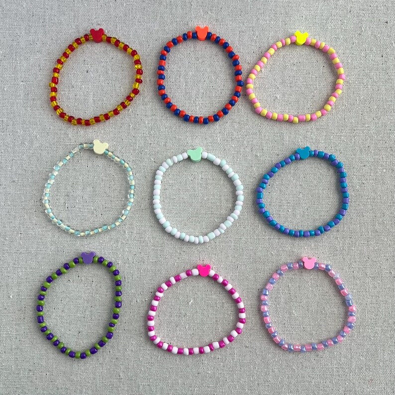 May include: Nine beaded bracelets in various colors, each with a small heart-shaped charm. The bracelets feature a variety of colors, including red, blue, yellow, green, and pink. The bracelets are displayed on a neutral-colored surface.