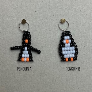May include: Two beaded penguin keychains, one with black and white beads and orange accents, the other with black and white beads and orange accents. The keychain on the left is labeled "Penguin A" and the keychain on the right is labeled "Penguin B".