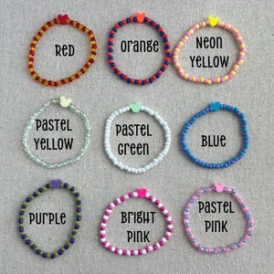 May include: Nine beaded bracelets in various colors, including red, orange, neon yellow, pastel yellow, pastel green, blue, purple, bright pink, and pastel pink. Each bracelet has a heart-shaped accent and a color-coordinated text label.