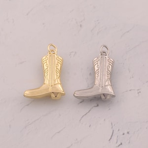 May include: Two metal charms shaped like cowboy boots, one in a polished gold tone and the other in a polished silver tone. Each boot charm features detailed embossed stitching patterns along the shaft and a small circular jump ring at the top.