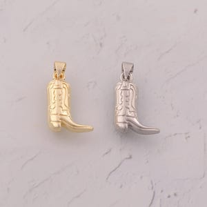 May include: Two pendants shaped like cowboy boots. One is gold-colored, the other is silver-colored. Each boot has a loop at the top for a chain. The boots are detailed with stitching and a pointed toe.