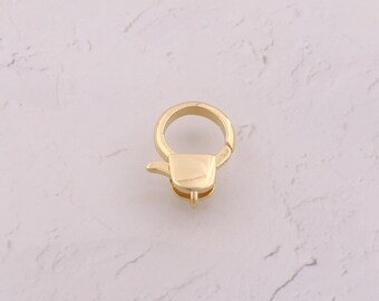 May include: A gold-colored swivel clasp, a hardware component, is shown against a white marble background. The clasp has a circular ring and a rectangular base with a small lever. The metal appears to be shiny and new.