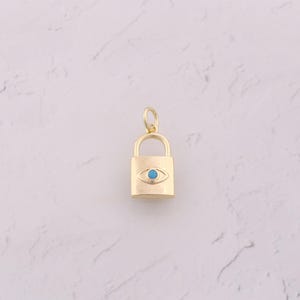 May include: A gold-colored padlock pendant with a turquoise eye design. The pendant is rectangular with rounded edges and a small loop at the top for a chain. The eye is centered on the padlock.