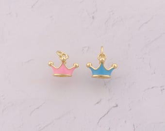 May include: Two gold-colored crown charms with colorful enamel details. One crown is pink, the other is blue. Both have a loop at the top for attaching to a necklace or bracelet. The crowns have a classic, regal design.