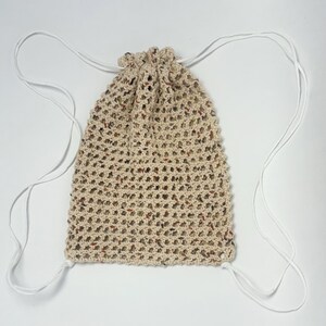 May include: A beige crocheted drawstring bag with white drawstrings. The bag has a speckled pattern with brown and orange flecks.