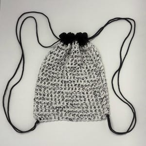 May include: A white and black crocheted drawstring bag with black drawstrings. The bag has a mesh-like pattern.