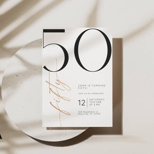 May include: A white rectangular invitation card featuring the large black number 50 at the top. The word fifty is written in a thin gold script font vertically. Text includes John is turning fifty, join us to celebrate, Saturday 12th Feb at 3 PM, and 123 Anywhere st, Any city, ST 12345.