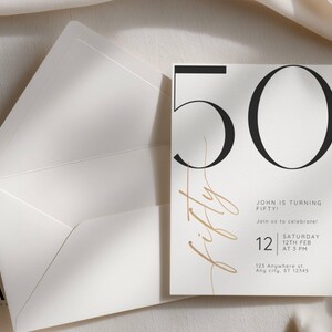 May include: A white invitation card with a large black number 50 and the word fifty in gold script. The text reads John is turning fifty, join us to celebrate, Saturday 12th Feb at 3 PM, and 123 Anywhere st, Any city, ST 12345. An open white envelope.