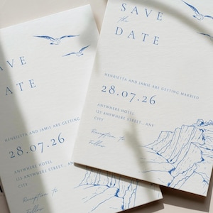 Puede incluir: Dos tarjetas Save the Date de color blanco roto con ilustraciones en tinta azul de gaviotas y acantilados costeros. El texto dice Save the Date, Henrietta and Jamie are getting married, 28.07.26, Anywhere Hotel, 123 Anywhere Street, Any City, Reception to Follow.