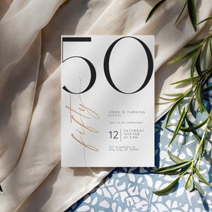 May include: A white rectangular invitation card featuring the large black number 50 and the word fifty in a thin gold script. The text reads John is turning fifty, join us to celebrate, Saturday 12th Feb at 3 PM, 123 Anywhere st, Any City, ST 12345.