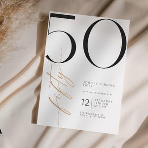 May include: A white rectangular invitation card featuring the large black number 50, the word fifty in a thin gold script font, and black text reading John is turning fifty, join us to celebrate, Saturday 12th Feb at 3 PM, 123 Anywhere st.