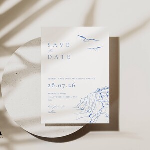 May include: A wedding invitation with navy blue text reading "Save the Date". The invitation includes the date, location, and names of the couple. The design features illustrations of seagulls and a coastal landscape.