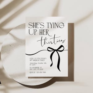 May include: A white invitation card with the text "SHE'S TYING UP HER thirties" in black script. A black bow graphic is below the text. The invitation is for a 40th birthday party.