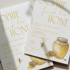 May include: Invitations for a bridal shower with the text "Sophie Found Her Honey." The design features a watercolor illustration of a honey jar, honey dipper, and bees. The invitation includes event details in a gold script font.