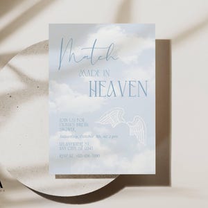 May include: A rectangular invitation card featuring a light blue sky with white clouds background. The text reads Match MADE IN HEAVEN, followed by details for Olivia's bridal shower on Saturday, October 5th, at 2 pm, with a white line drawing of wings.