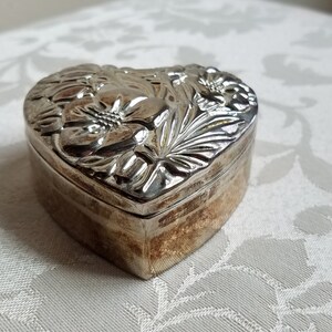 Puede incluir: Una caja de coraz&oacute;n de plata con un dise&ntilde;o floral en relieve.