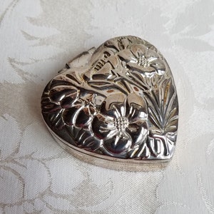 Puede incluir: Una caja de coraz&oacute;n de plata con un dise&ntilde;o floral. La caja est&aacute; cerrada y tiene una tapa con bisagras.