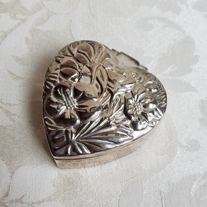 Puede incluir: Una caja de coraz&oacute;n de plata con un dise&ntilde;o floral en relieve.